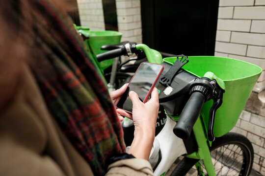 Woman using smartphone app for urban bike-sharing service - Powered by Adobe