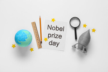 Fototapeta premium Paper with text NOBEL PRIZE DAY, earth model, rocket and stationery on white background