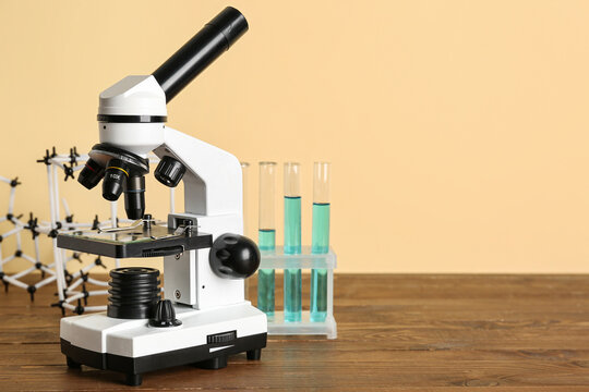 Microscope with test tubes of samples and molecular model on wooden table against beige background. Nobel Prize Day - Powered by Adobe