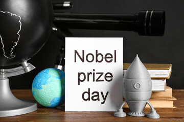 Fototapeta premium Paper with text NOBEL PRIZE DAY, globe, rocket and earth model on tile against grey background