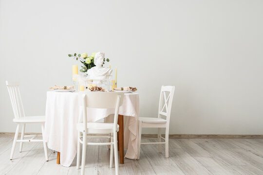 Table setting for Nobel prize day with Greek statuette and roses in light room