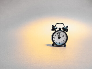 A small retro-style alarm clock stands alone under a warm spotlight, creating a calm and minimalist scene that symbolizes time, focus, and simplicity.