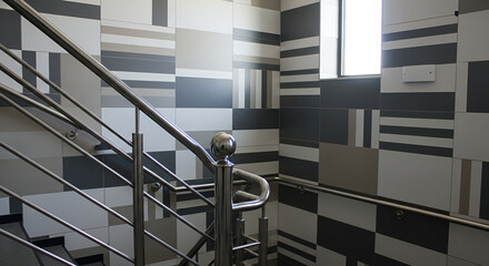 Image depicts a modern architectural interior featuring a staircase with sleek, metallic railings. The railings are polished and reflective, with a prominent spherical finial at the top of the newel p