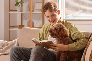 Young man reading book with cute Toy Poodle on sofa at home