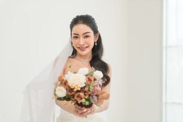 Asian bride in elegant white wedding dress holding bouquet. smiling, Romantic bridal portrait with graceful and classic style.