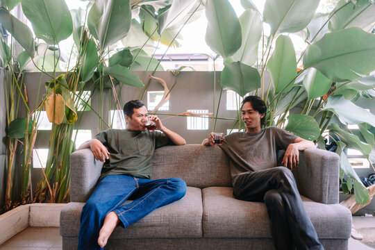Young Asian men relaxing on a sofa, enjoying drinks and conversation