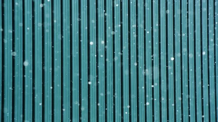 Delicate snowflakes drift past a textured industrial wall in crisp daylight