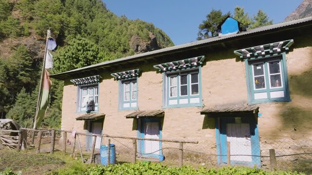 Drone rising over a teahouse, revealing a river town between mountains of Nepal