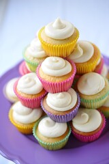 Colorful cupcakes with white frosting stacked on a purple plate for a party treat