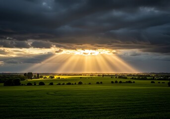 Dramatic sunlight piercing through dark clouds over green fields