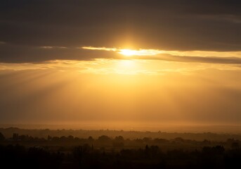 Obraz premium Dramatic sunrise illuminates landscape with golden light and atmospheric clouds