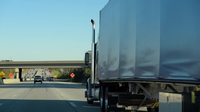 Semi truck hauls cargo along a busy interstate highway on a clear day. The trailer moves steadily through traffic, long haul trucking, logistics, supply chain operations