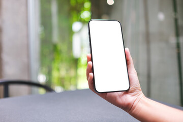 Mockup image of a woman holding and using mobile phone with blank desktop screen in cafe