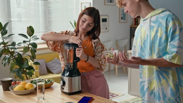 Teen brother and sister standing at kitchen counter cooking healthy smoothie with kiwifruit, using blender