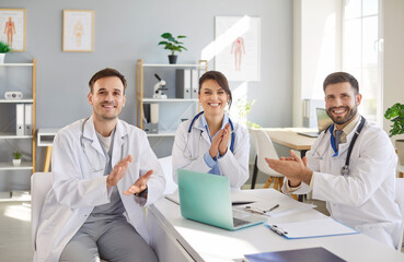 Obraz premium Portrait of a team of doctors and nurses gathered around the table in a hospital office, celebrating success and applauding together. Teamwork, achievement, and a joyful atmosphere.