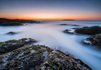 Breathtaking twilight seascape with ethereal water flowing around mossy rocks - feel the peace, perfect for travel blogs, nature prints, and mindfulness apps