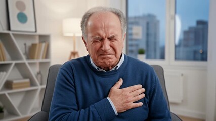 An elderly man sits in a warm living room, holding his chest in distress. He appears troubled and in pain, seeking comfort in his familiar surroundings