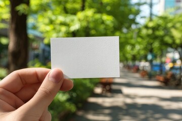 Hand holding blank white business card with blurred green background  