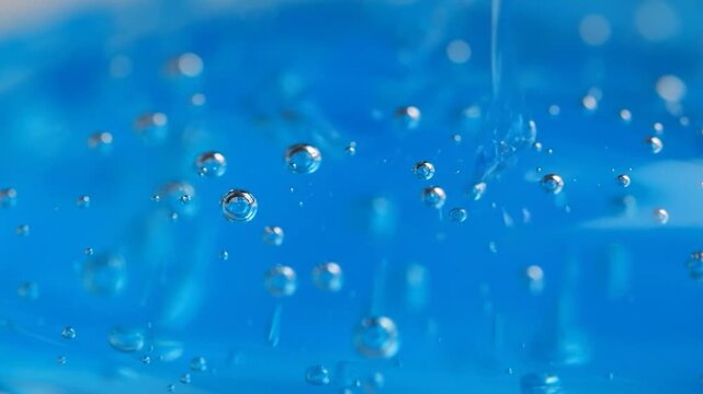 Macro photo of transparent bubbles floating in a bright, saturated, blue liquid, with a soft blur