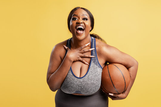 Happy, excited African American woman wearing stylish sportwear holding basketball