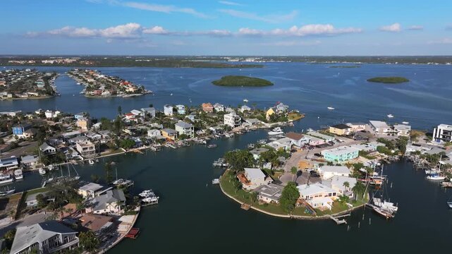 Aerial drone establishing shot of luxury waterfront neighborhood along Boca Ciega Bay near Jack's Boat Basin, featuring colorful homes with private docks on a canal in Saint Pete Beach, Florida.