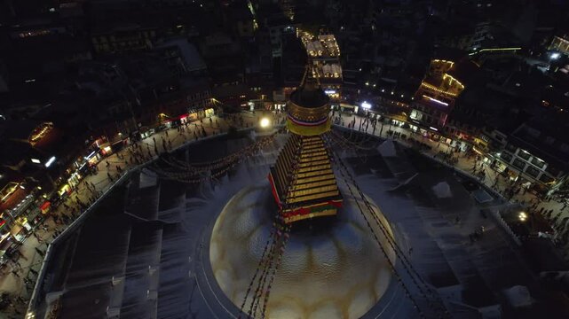 A serene night drone view of Boudhanath Stupa, also known as boudha nath, glowing above Kathmandu. The sacred Buddhist landmark stands radiant against the quiet urban nightscape.