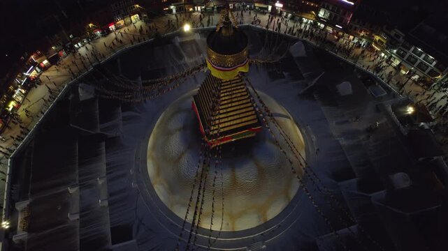 A serene night drone view of Boudhanath Stupa, also known as boudha nath, glowing above Kathmandu. The sacred Buddhist landmark stands radiant against the quiet urban nightscape.