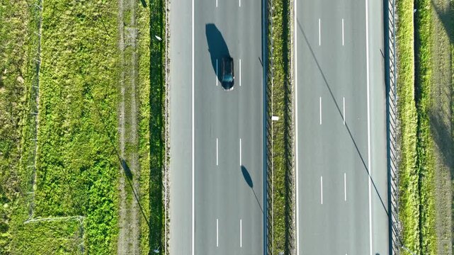 Aerial perspective of two parallel highway sections with cars moving in opposite directions under bright sunlight.
