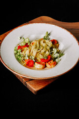 Shrimp fettuccine served on a wooden plate with fresh vegetables and herbs