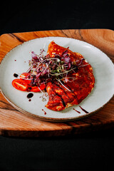 Delicious omelette topped with greens and tomatoes on a wooden plate
