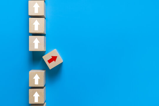 wooden blocks with up white arrows and one different direction red arrow isolated on blue background. leadership concept