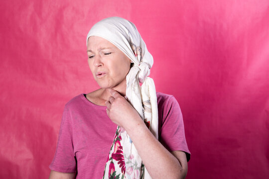 Portrait of a woman wearing a headscarf, commonly associated with cancer treatment, gently touching her throat with an expression suggesting discomfort from radiotherapy side effects. 