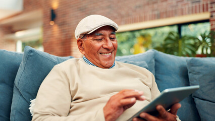 Tablet, happy and senior man on sofa in home with networking, social media or blog post. Relax,...