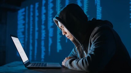 Hacker in hood uses laptop for cyber attack with code display. Person hacking computer for cybercrime. Hacker works on laptop at night. Cyber security breach with hooded hacker using computer. - Powered by Adobe