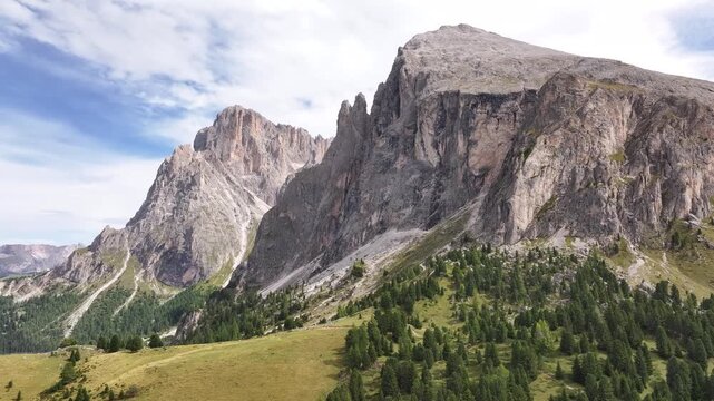Drone flight along the Langkofel mountain massif in the Dolomites. At its foot, alpine meadows and pine forests can be seen.