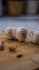 Close-up of a mesh bag filled with whole garlic bulbs placed on a wooden cutting board. Shallow depth of field with blurred background, creating a rustic kitchen atmosphere.”