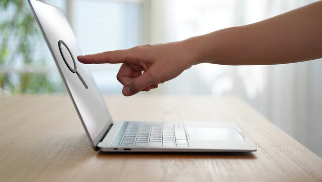 Close-up of Hand Touching Magnifying Glass Icon on Laptop Screen Displaying Search Functionality and User Interaction with Technology - Powered by Adobe