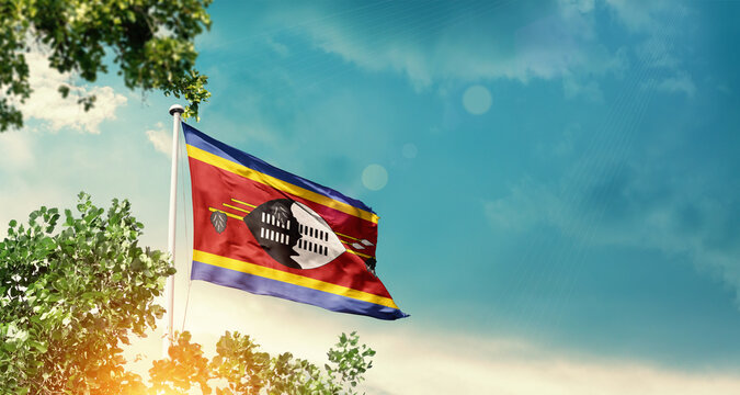 Eswatini national flag waving in the sky behind the tree. The flag blowing with beautiful sunlight. Eswatini national flag for independence day. - Powered by Adobe
