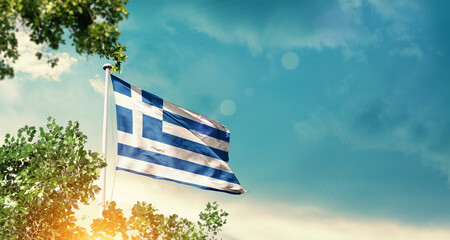 Greece national flag waving in the sky behind the tree. The flag blowing with beautiful sunlight. Greece national flag for independence day.