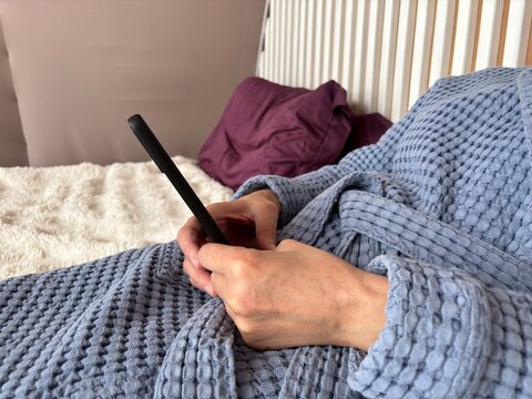 Mature brunette woman with under-eye patches working on a smartphone at home, chatting and freelancing while relaxing and combining skincare with remote work.