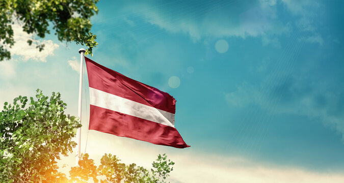 Latvia national flag waving in the sky behind the tree. The flag blowing with beautiful sunlight. Latvia national flag for independence day.