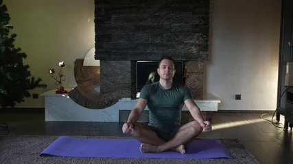 Fotobehang Lotusbloem A man exercising at home. Fitness and exercise at home. A man in the lotus position on a yoga mat.  © OlTarakanov
