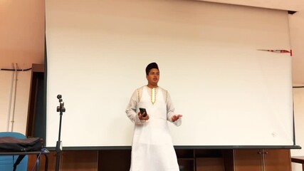 A focused Muslim student sits at a desk in a classroom, reading, thinking, and writing notes. The scene captures concentration, learning, and academic dedication in a bright educational environment. 