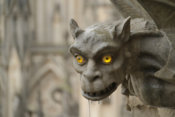 A close-up of a stone gargoyle statue with glowing yellow eyes, giving it a menacing and supernatural look.