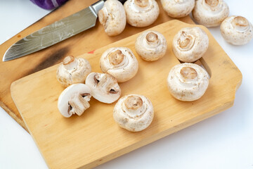 Whole and sliced button mushrooms on a rustic wooden cutting board with a chef's knife. Preparation shot for cooking, recipe, and culinary concepts, viewed from above.