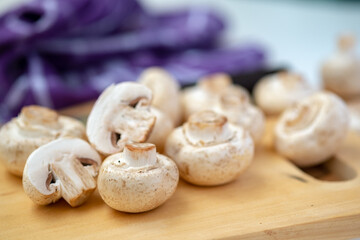 Shallow depth-of-field close-up of whole and halved button mushrooms on a wooden board. Focus on foreground detail, texture, and preparation for cooking concepts.