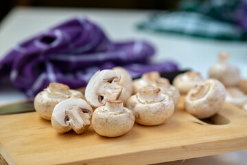 Shallow depth-of-field close-up of whole and halved button mushrooms on a wooden board. Focus on foreground detail, texture, and preparation for cooking concepts.