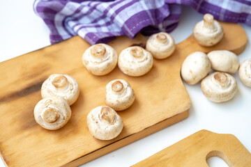 Arrangement of whole and sliced button mushrooms on a wooden cutting board, with a purple cloth and knife in the background. Overhead shot for cooking and kitchen concepts.