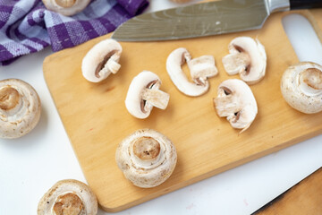 Whole and sliced button mushrooms on a rustic wooden cutting board with a chef's knife. Preparation shot for cooking, recipe, and culinary concepts, viewed from above.
