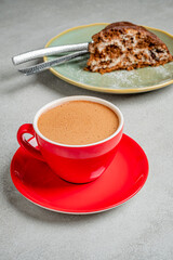 A vibrant red cup filled with rich coffee sits next to a slice of chocolate cake on a plate